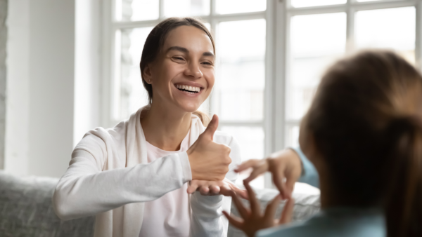 A smiling female wearing a white hoodie uses ASL to communicate.