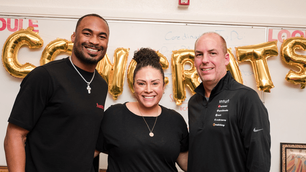 Two men and a woman pose in front of a string of gold 'congrats' ballons.