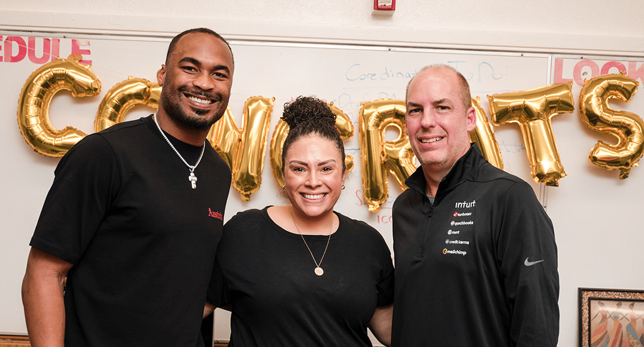 Two men and a woman pose in front of a string of gold 'congrats' ballons.