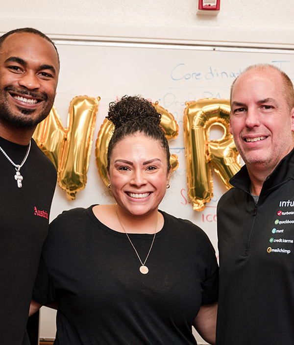 Two men and a woman pose in front of a string of gold 'congrats' ballons.