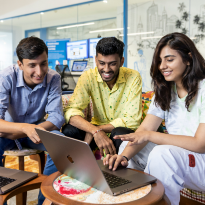 A group of Indian technology professionals collaborate around a laptop in a corporate office.