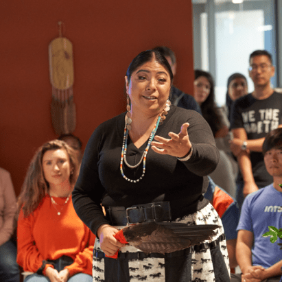 An Indigenous woman performs a blessing ceremony to employees in an office.