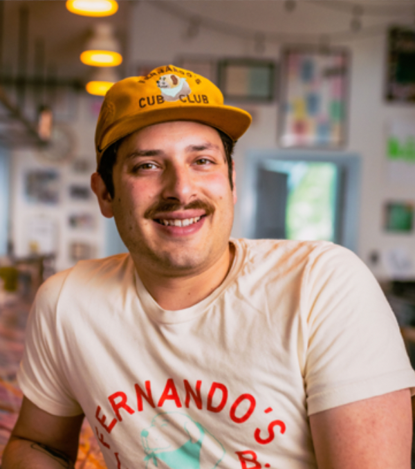 Brunette man with hat sits behind counter in restaurant.